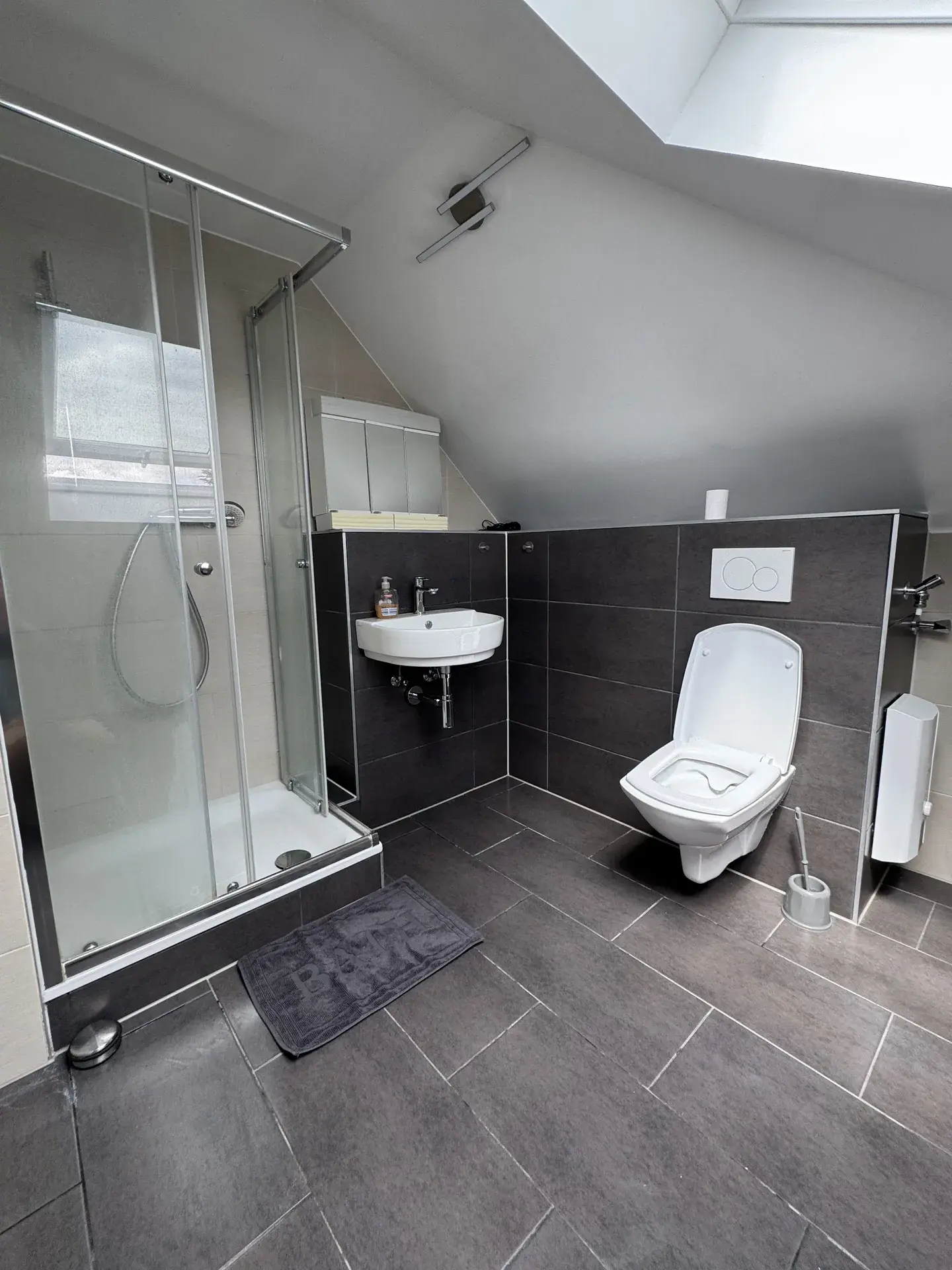 Modernes Bad des Monteurzimmers bei Lich mit Glasdusche, WC und Waschtisch unter der Dachschräge